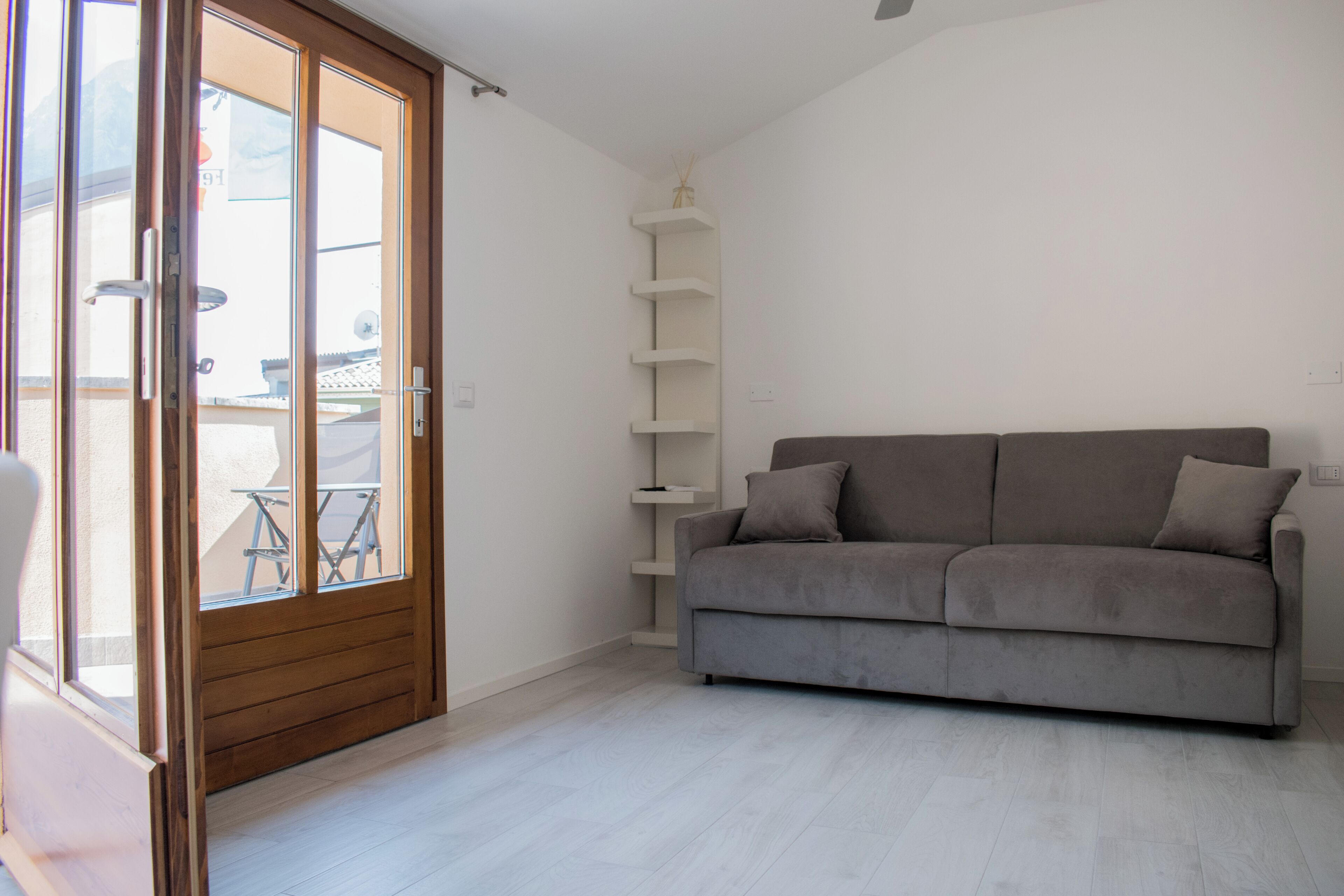 Una sala de estar con un sofá gris, una puerta de madera y un estante blanco.