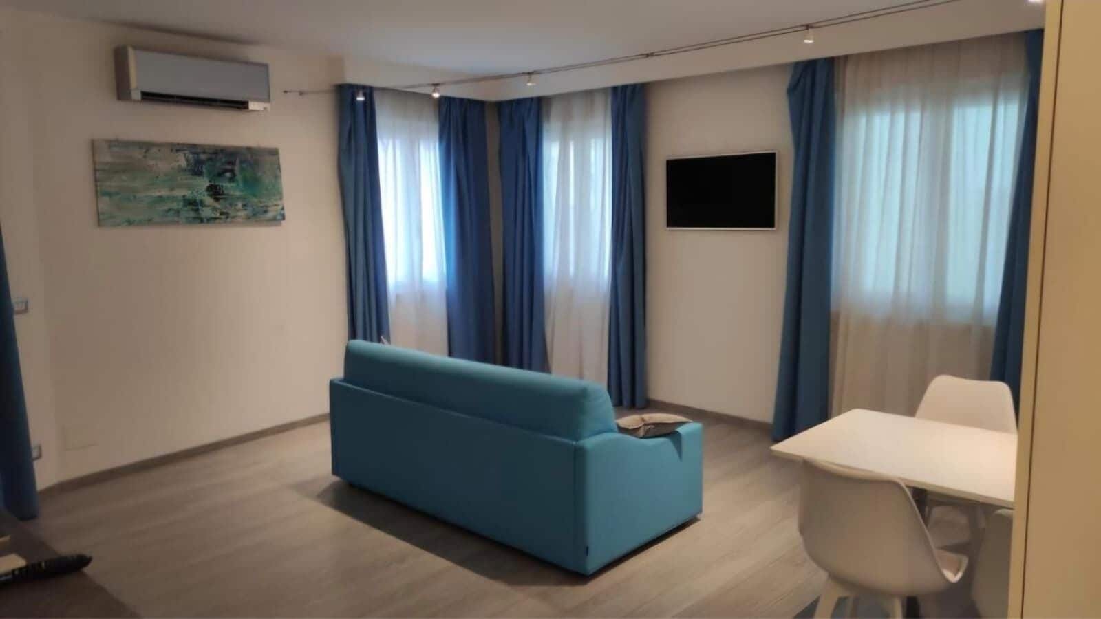 Un salon moderne avec un canapé bleu, une table blanche et un téléviseur à écran plat fixé au mur.