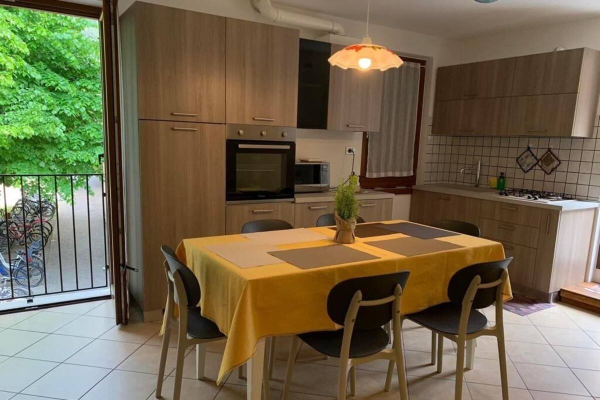 A modern kitchen with wooden cabinets, a dining table with chairs, and a balcony with bicycles.