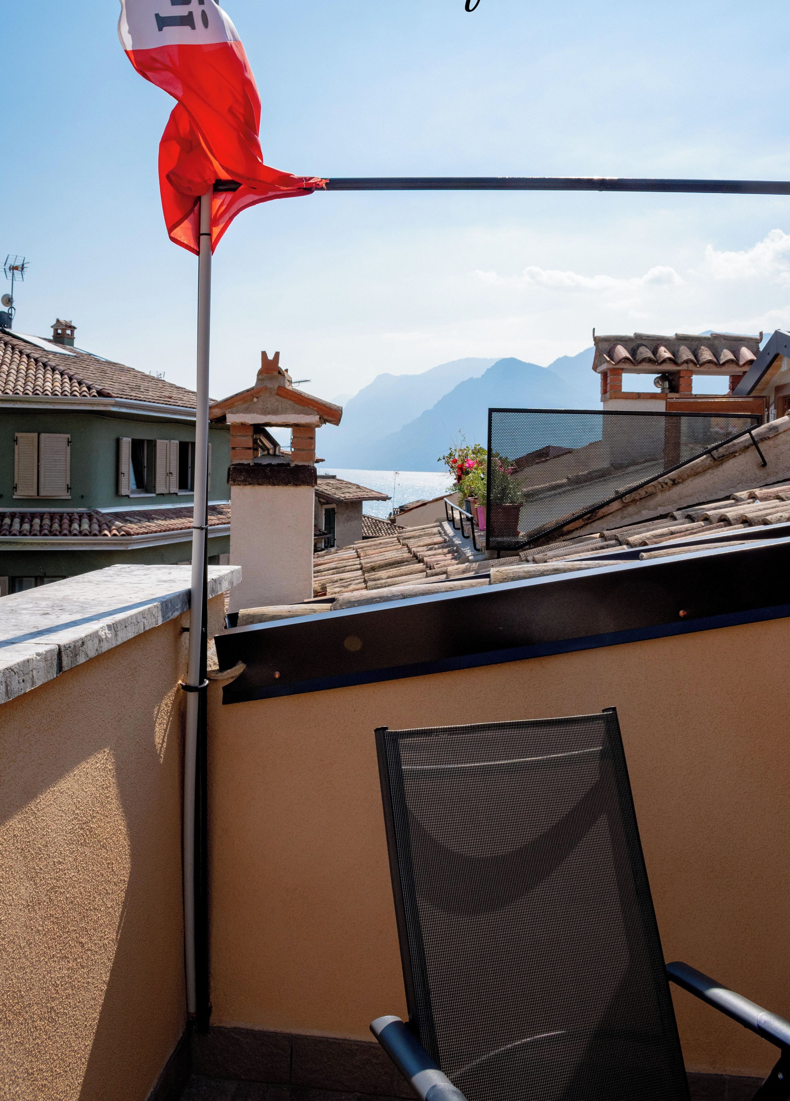 Un balcón con una bandera roja, una silla y vistas al mar y las montañas.