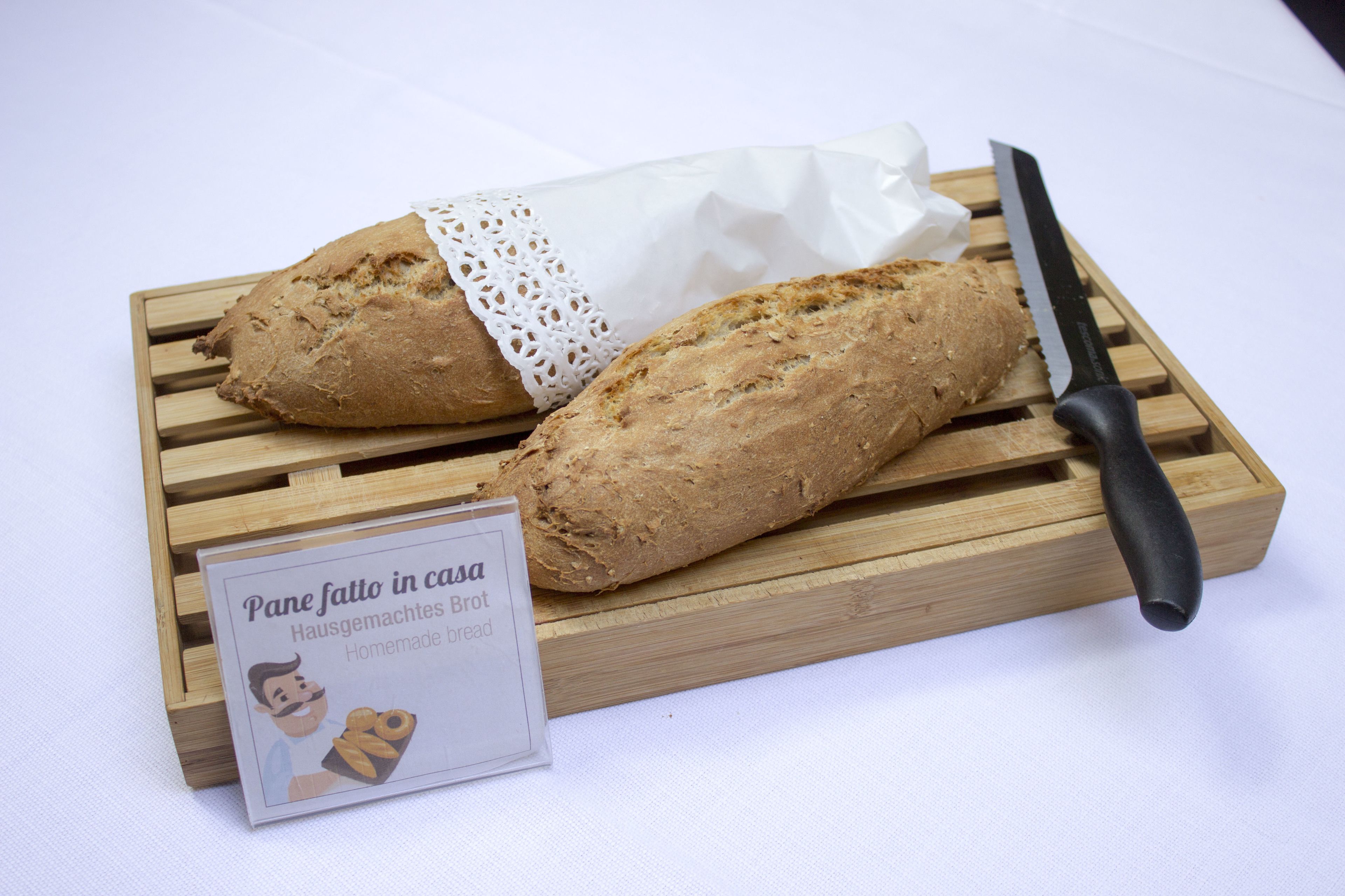 Two loaves of bread on a wooden cutting board with a knife and a sign indicating 'Pane fatto in casa'.
