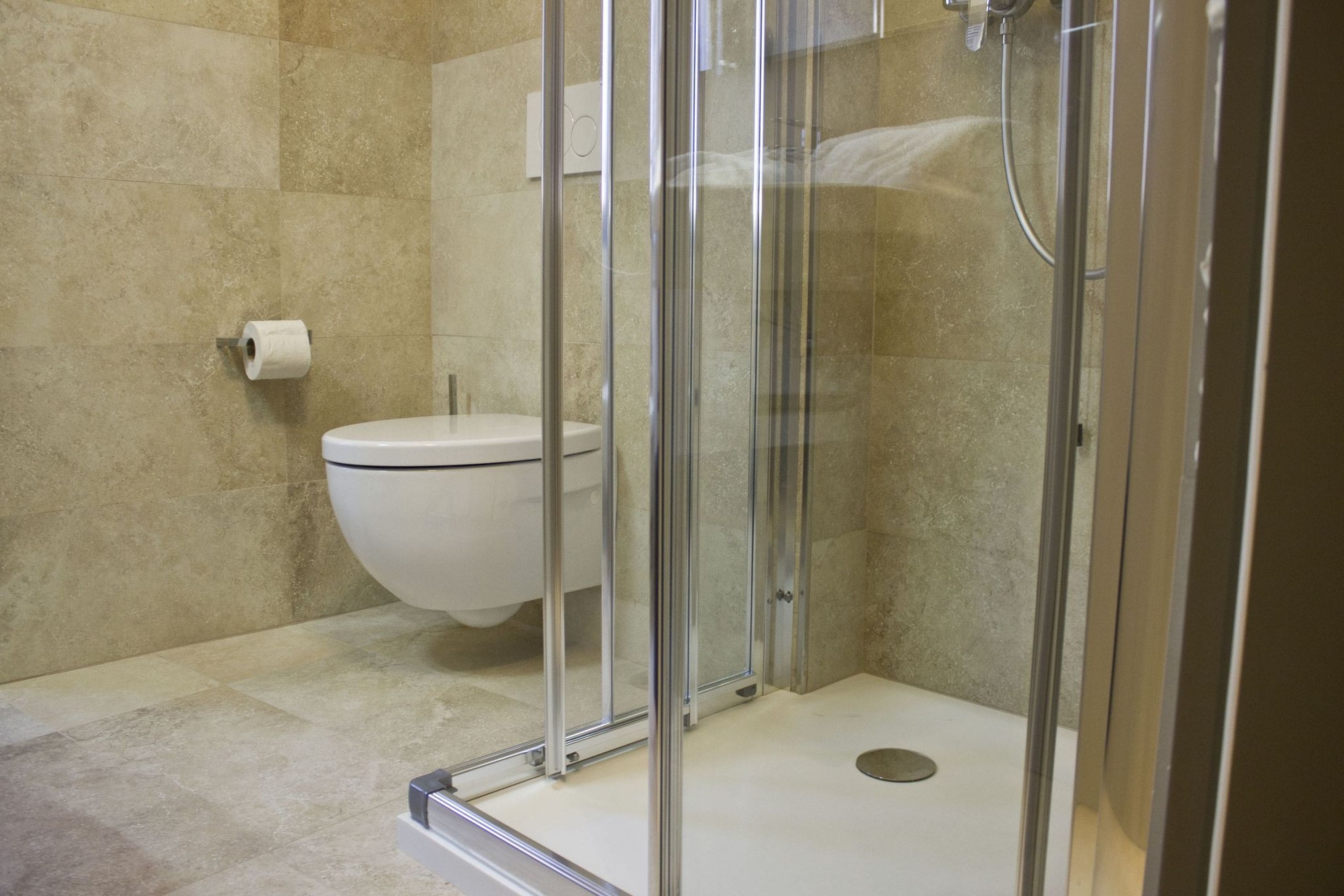 A modern bathroom with a glass-enclosed shower, a toilet, and a roll of toilet paper on the wall.