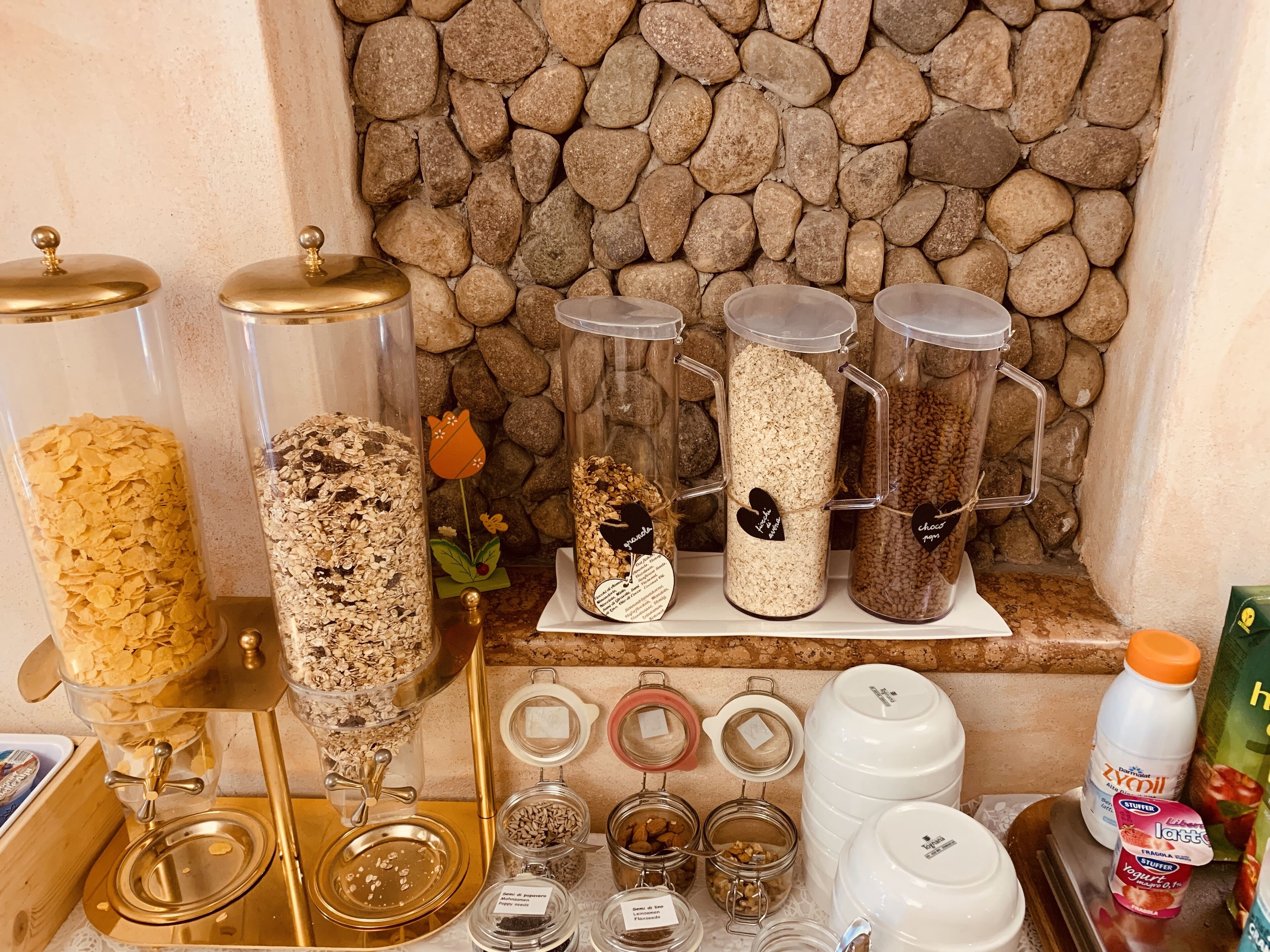 Zona cuina amb diferents recipients per guardar aliments, incloent pots i dosificadors, i una paret de pedra al fons.