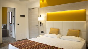 Una habitación de hotel con una cama grande, una mesita de noche, una lámpara de pared y una puerta que da a otra habitación.