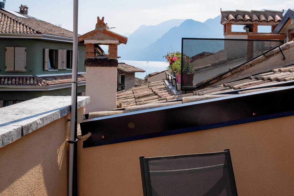 A balcony with a red flag, a chair, and a view of a mountain and water.