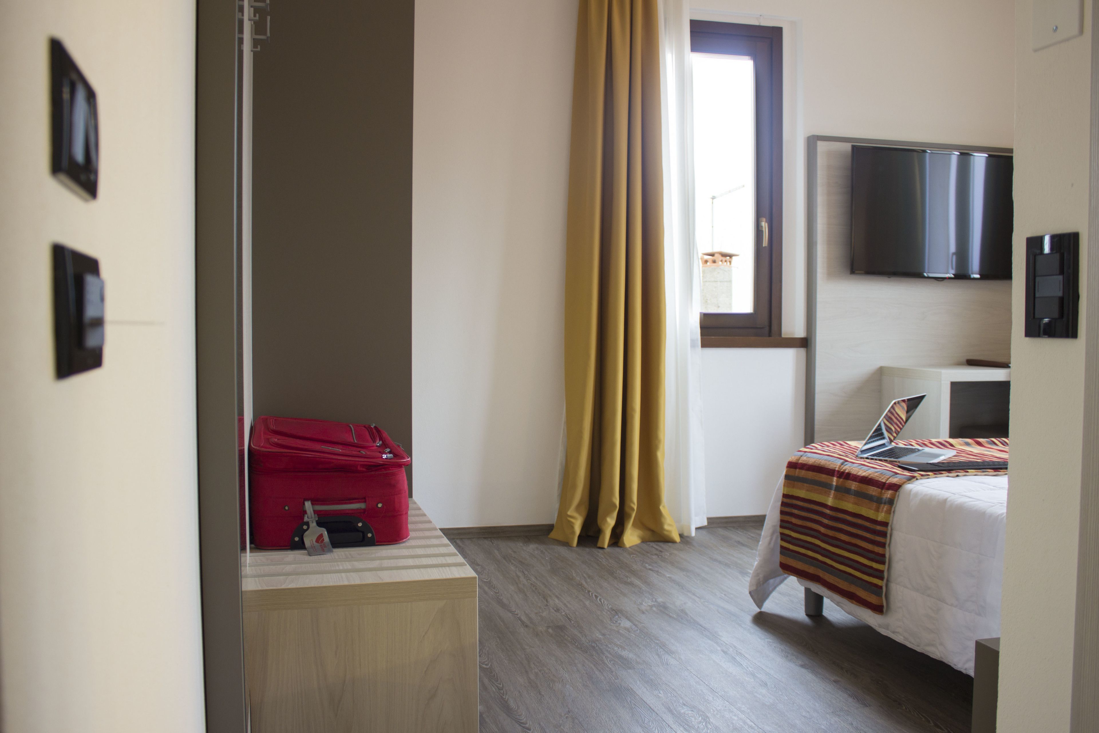 Une chambre d’hôtel avec un lit, un bureau, une télévision et une valise posée sur le bureau.