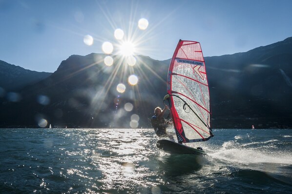 A person windsurfing on a lake with mountains in the background.