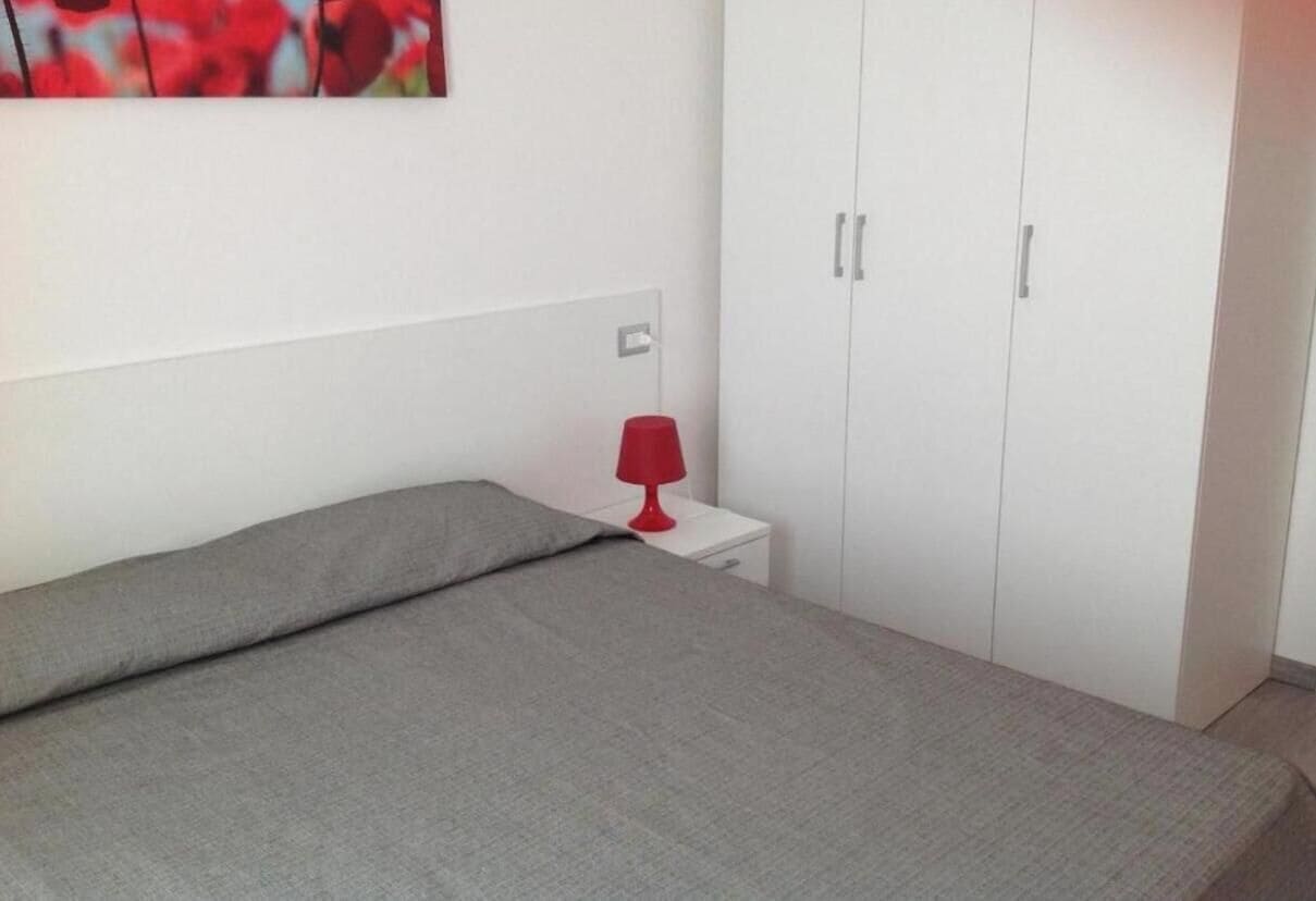Un dormitorio con cama, mesita de noche, lámpara roja y armario.