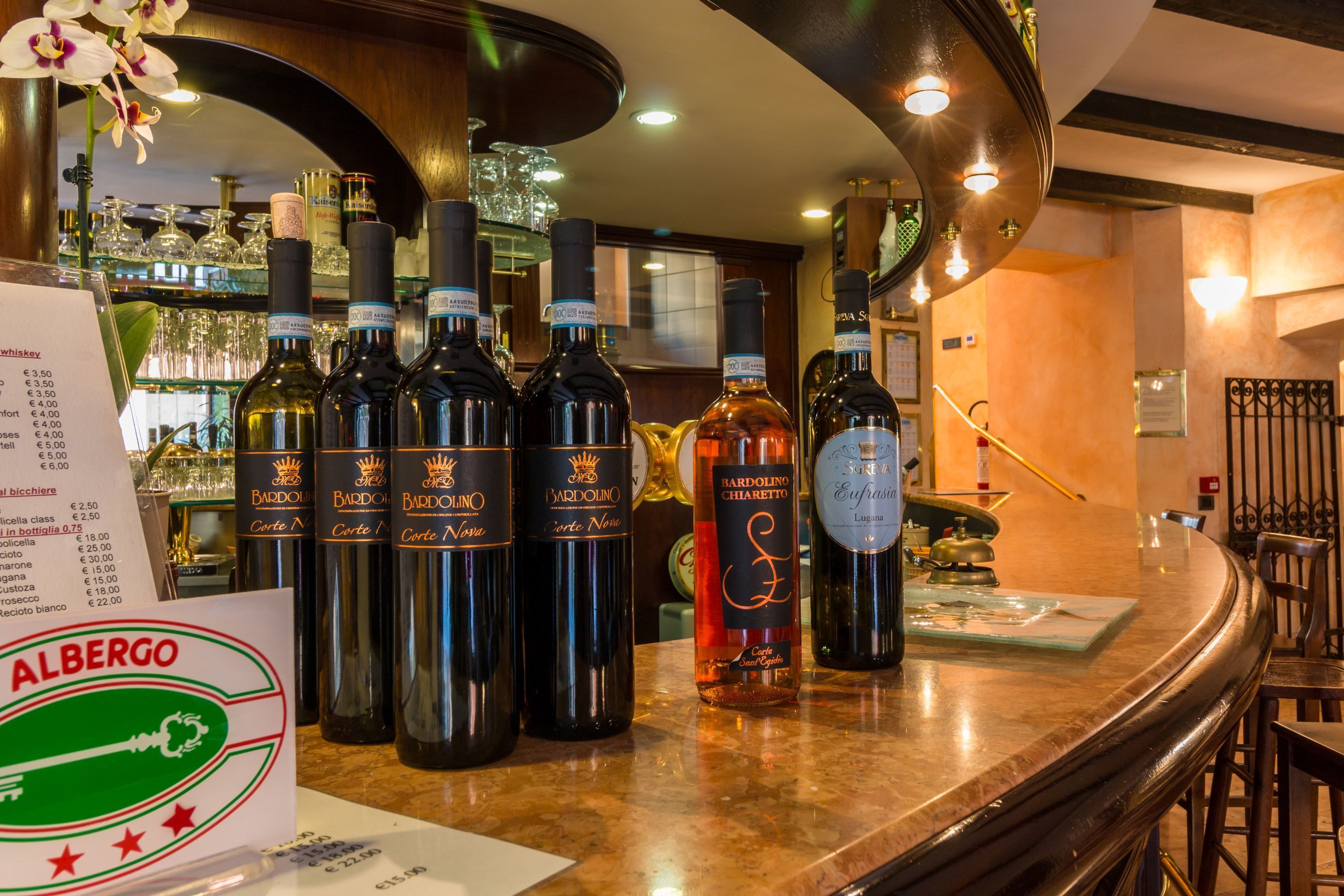 Un espace bar avec plusieurs bouteilles de vin Bardolino et un panneau affichant le menu.