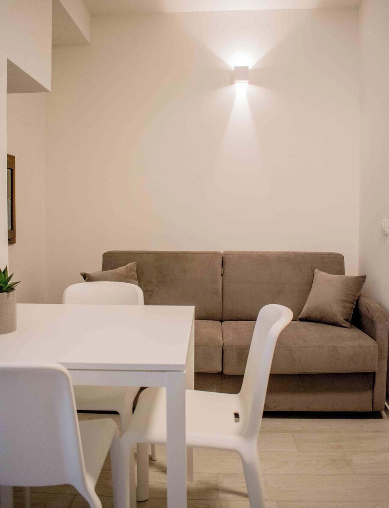 Un soggiorno dal design minimalista con un tavolo bianco, due sedie bianche, un divano beige e una lampada da terra.