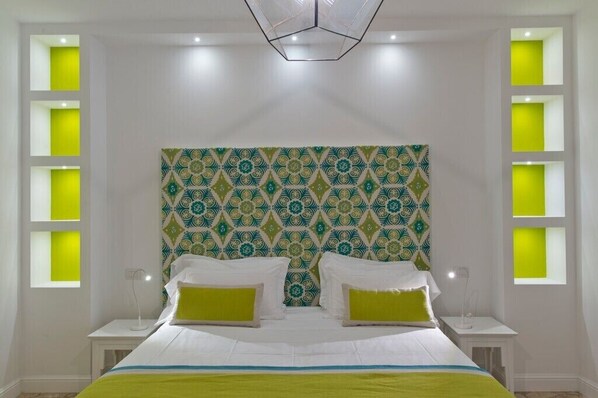 A modern bedroom with a patterned headboard, two bedside tables with lamps, and a green accent pillow. - Stella Marina Praiano (Praiano)