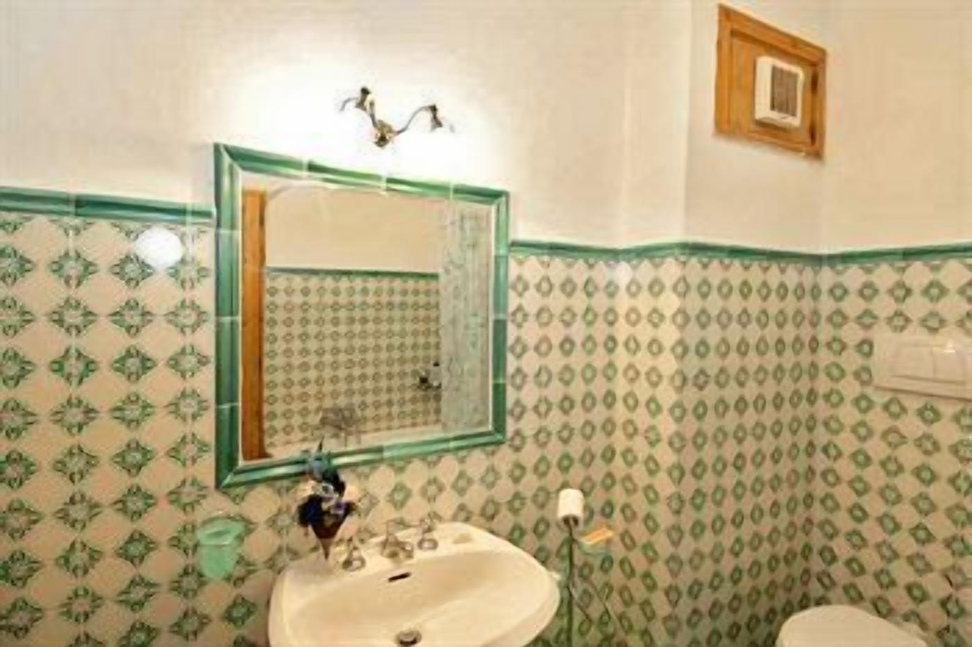 Un baño con papel tapiz estampado, un lavamanos, un espejo y una lámpara.