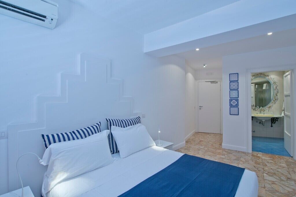 Un dormitorio con cama, paredes blancas, un baño con espejo y lavabo, y una escalera.