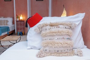 Una cama con un almohadón blanco y un cojín decorativo con flecos.
