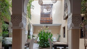 An indoor courtyard with a dining area, ornate columns, hanging lanterns, and a decorative window.