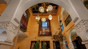 An interior with a central wooden door, white decorative arches, hanging lanterns, and potted plants.