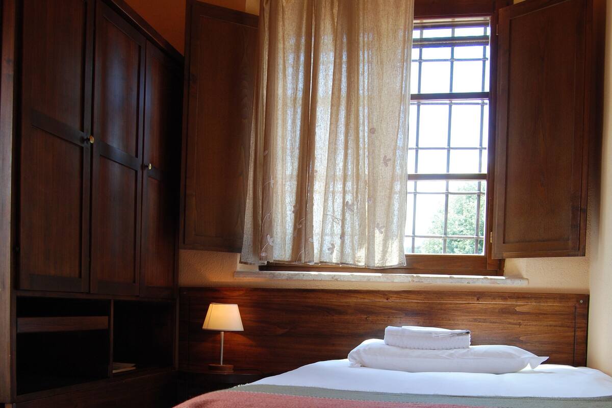A bedroom with a bed, a window with curtains, a lamp, and wooden furniture.