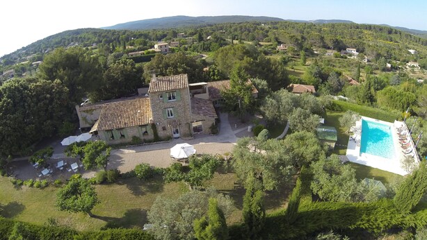Vista aérea de una propiedad con una casa de piedra, una piscina y vegetación circundante.