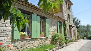 Un edificio de piedra con contraventanas verdes y jardineras con flores en las ventanas.