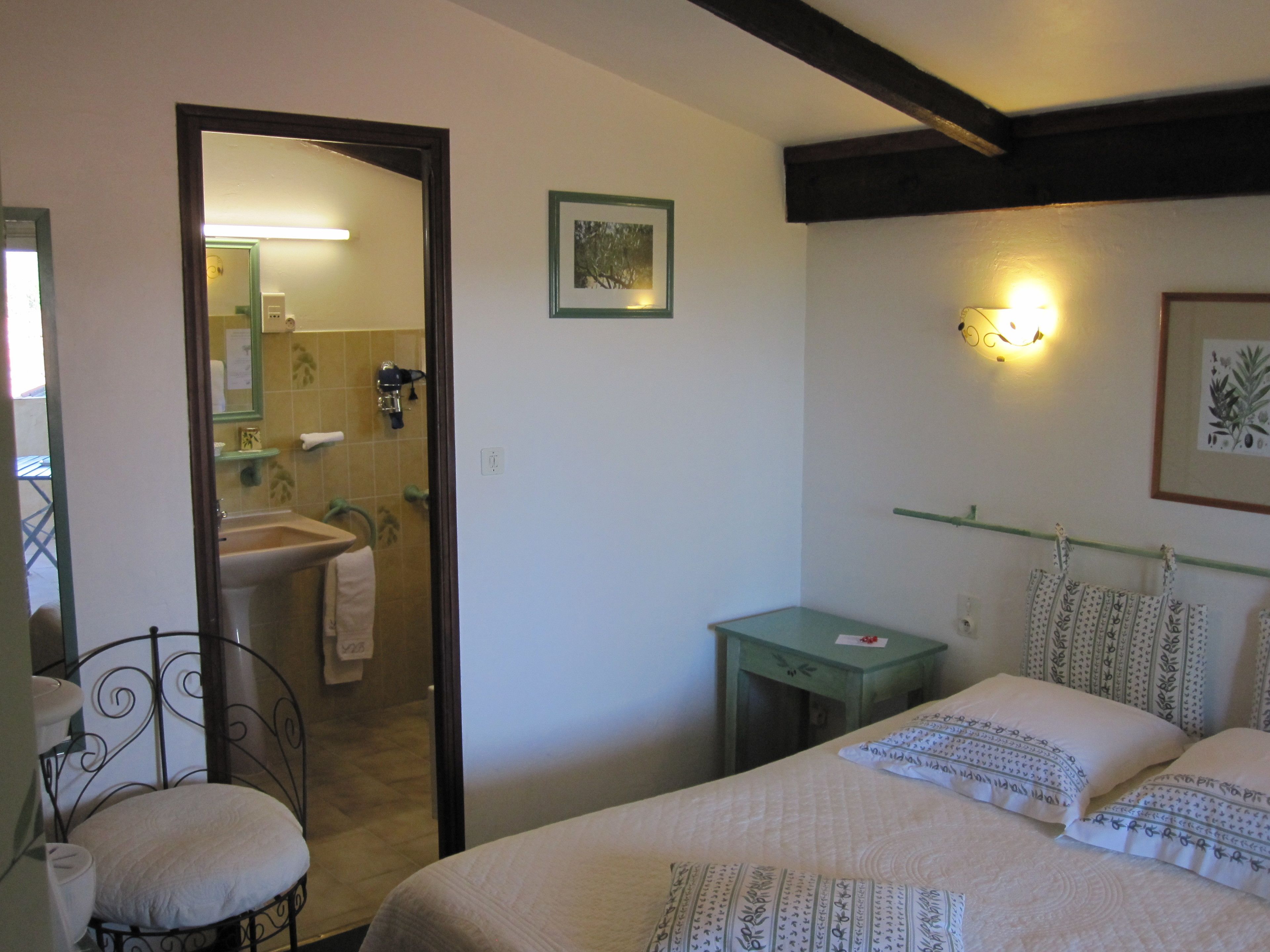 A bedroom with a bed, a bedside table, a chair, a mirror, and a bathroom visible through an open door.