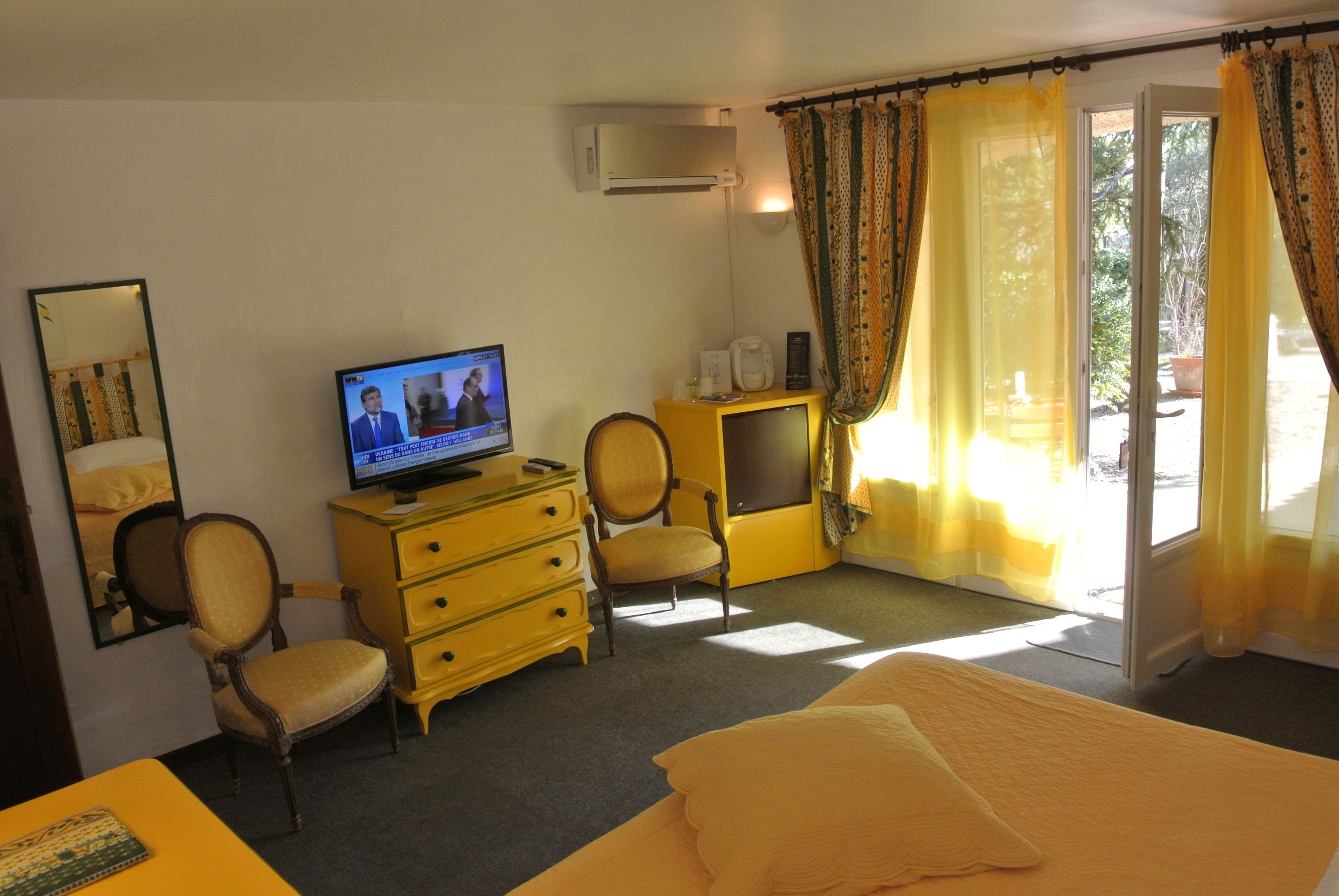 Une chambre d’hôtel avec un lit, un téléviseur diffusant un programme d’information, une chaise, une commode et une fenêtre avec des rideaux.