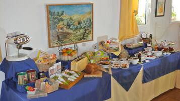 Una mesa de buffet con diversos alimentos y condimentos, un cuadro en la pared y una ventana con cortinas.