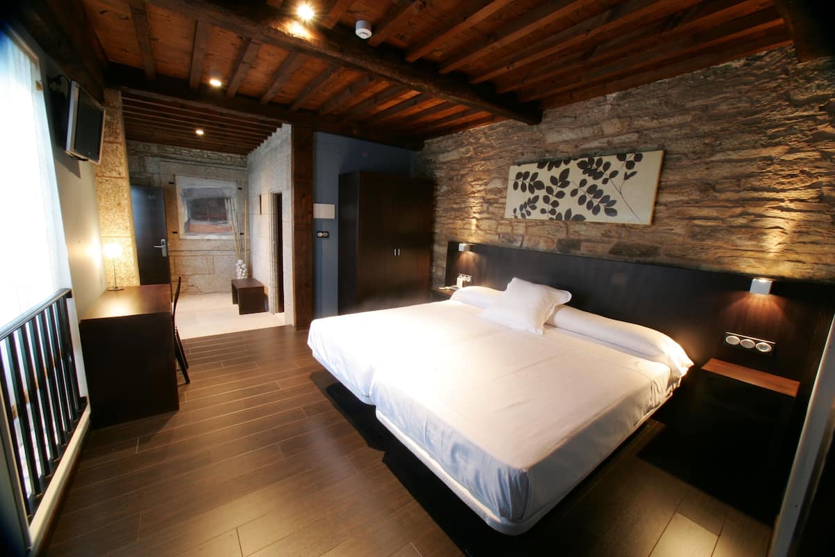 A bedroom with a large bed, wooden floor, stone wall, and a mounted TV.