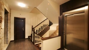 A modern hallway with a wooden staircase, a door labeled "101", and a stainless steel elevator. - A Tafona do Peregrino (Santiago de Compostela)