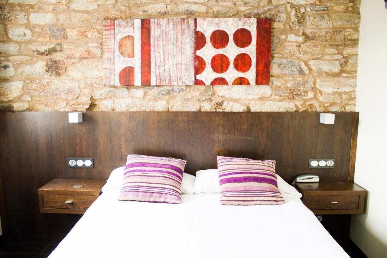 Een hotelkamer met een stenen muur, een houten hoofdeinde, twee nachtkastjes met lampen en een bed met gestreepte kussens.