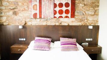 Een hotelkamer met een stenen muur, een houten hoofdeinde, twee nachtkastjes met lampen en een bed met gestreepte kussens.