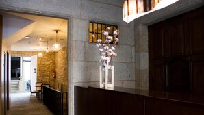 A reception area with a stone wall, a wooden reception desk, and a hanging cotton plant. - A Tafona do Peregrino (Santiago de Compostela)