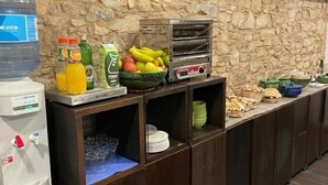 A buffet setup with a water dispenser, beverages, fruits, a bread oven, and various food items. - A Tafona do Peregrino (Santiago de Compostela)