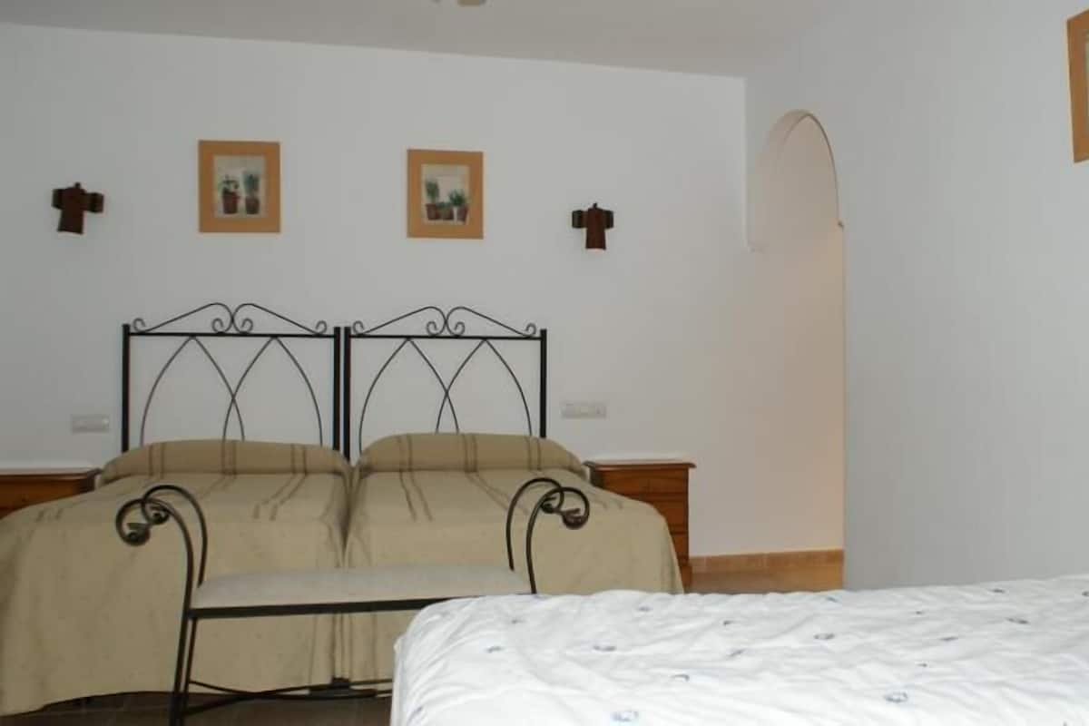 A bedroom with a double bed, a single bed, a metal-framed headboard, and two wall-mounted picture frames.