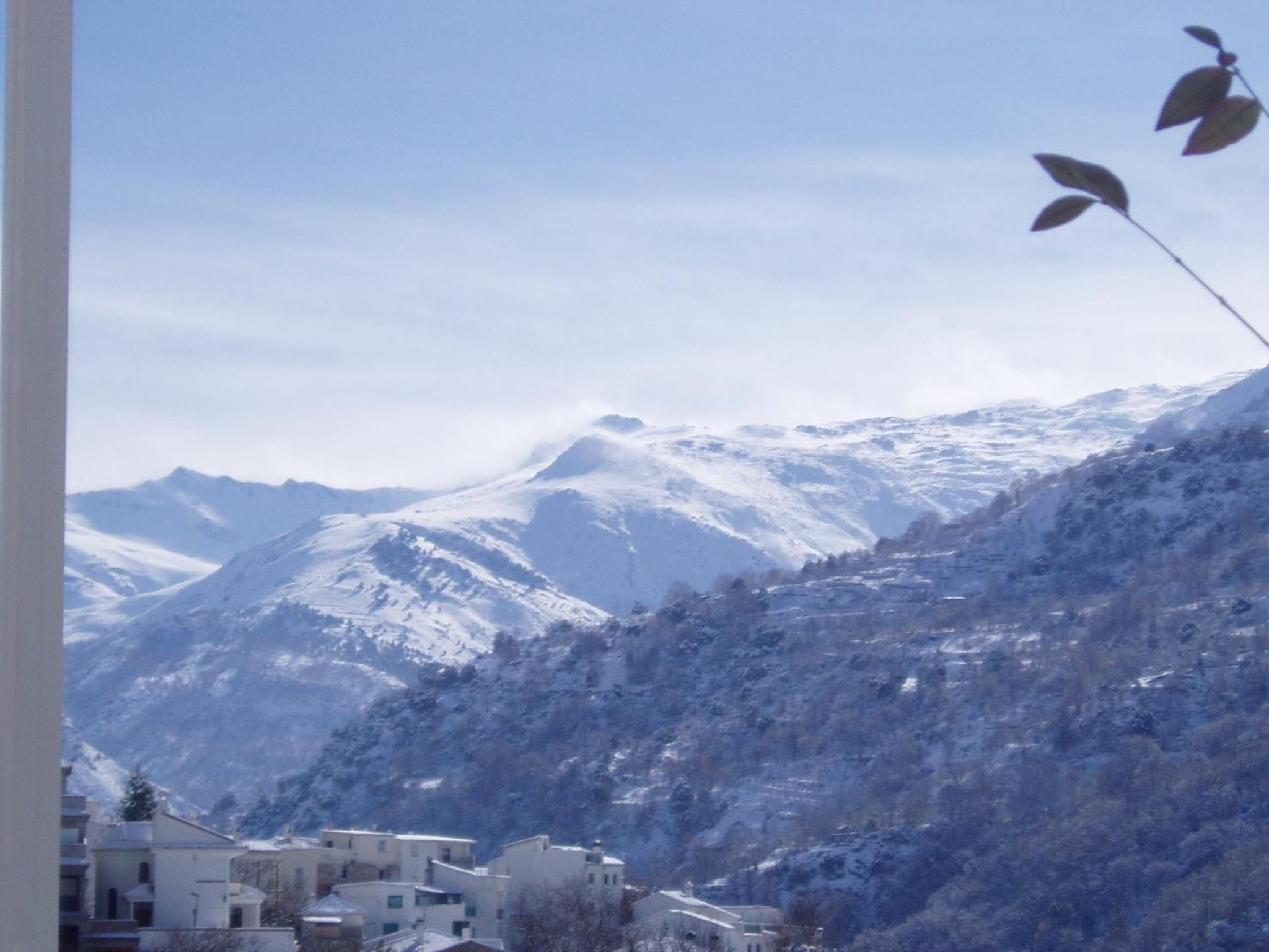 A mountainous landscape with snow-covered peaks and a small settlement with buildings.