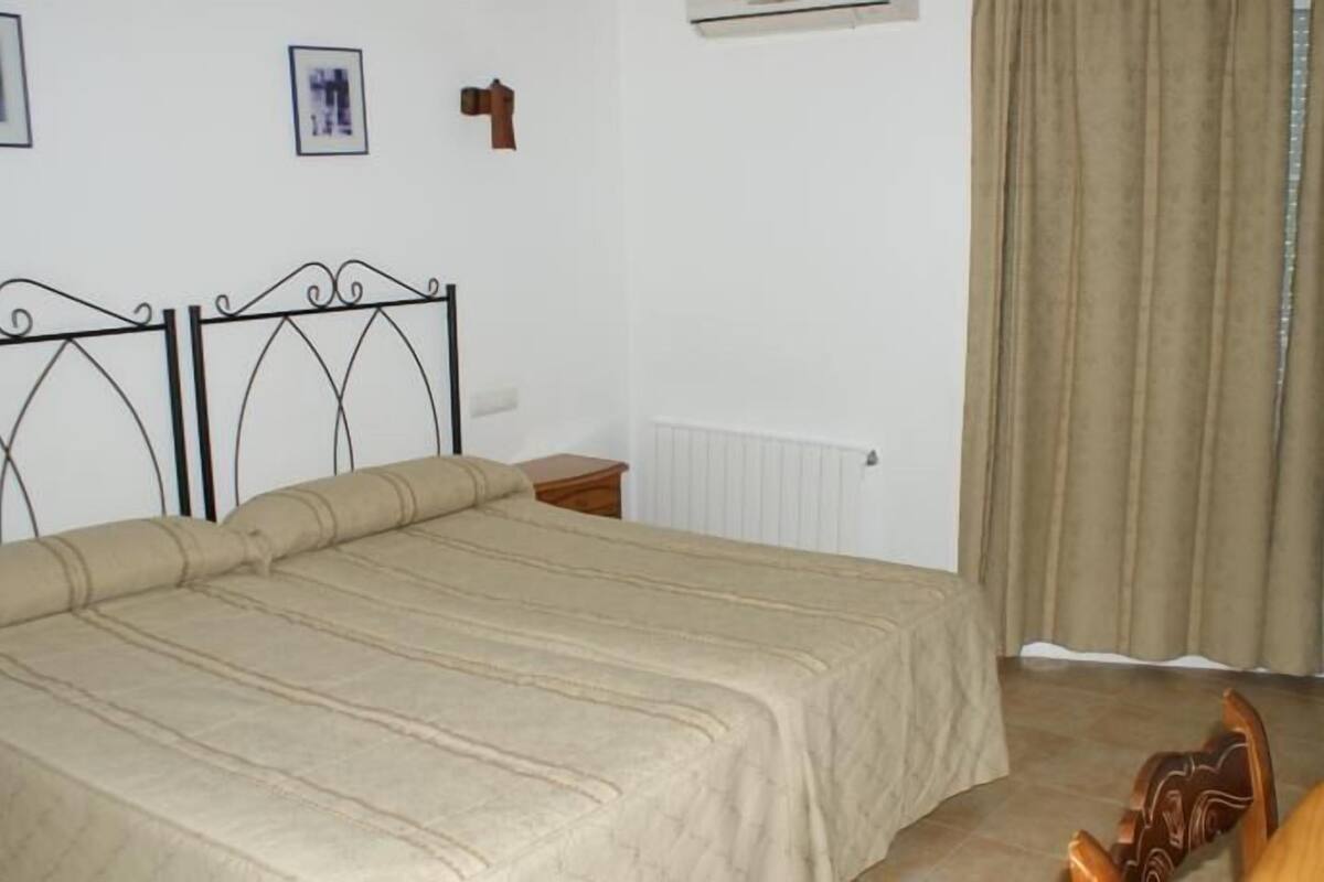 A bedroom with a bed, a chair, a nightstand, a radiator, and a window with curtains.