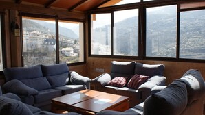 A living room with two sofas and a coffee table, large windows with a mountain view, and a wooden ceiling. - Juan Francisco (Guejar Sierra)