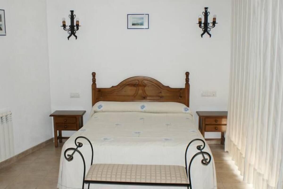 A bedroom with a wooden bed, two bedside tables, a radiator, and two wall-mounted lamps.