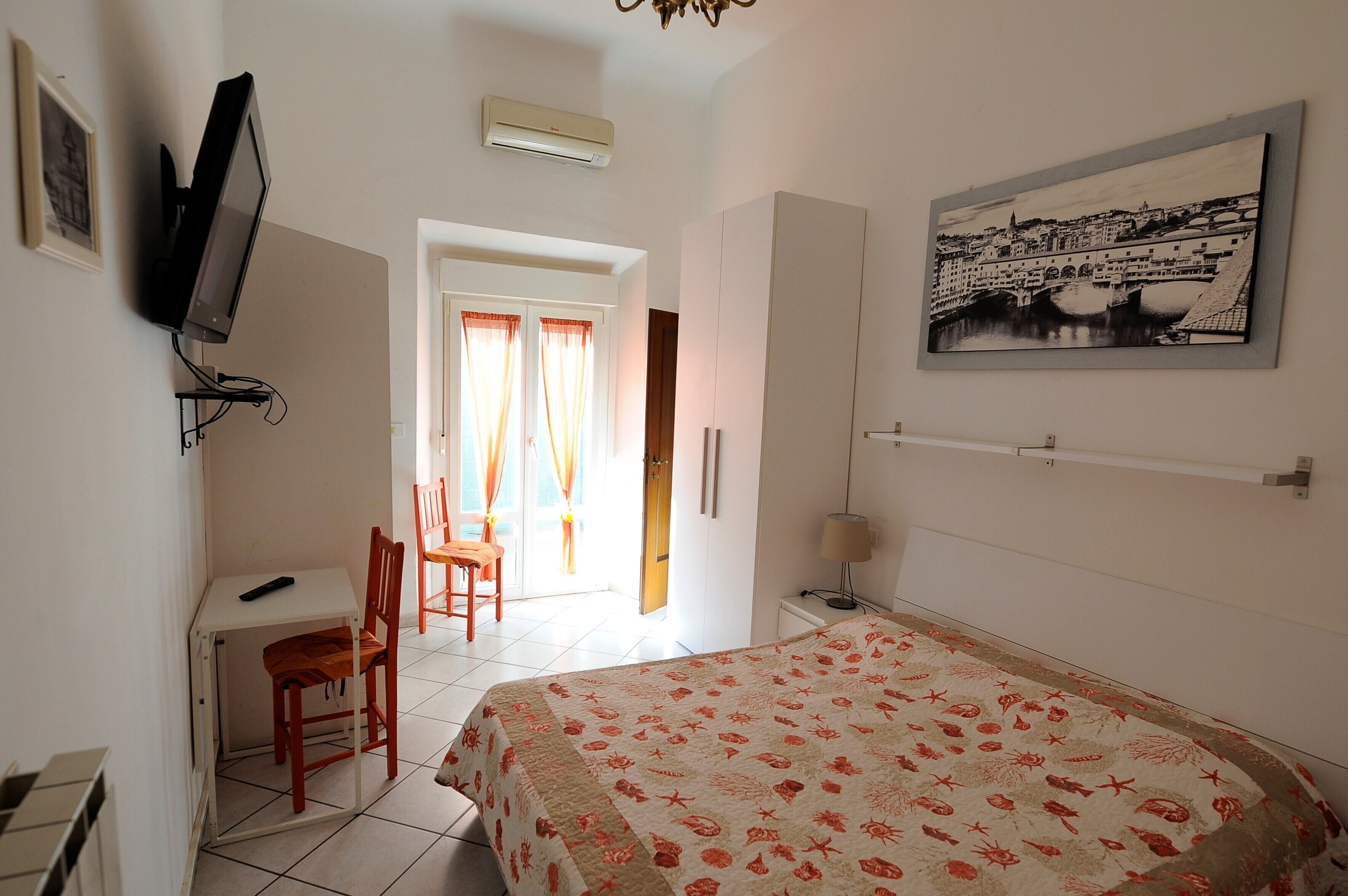 Un dormitorio con cama, escritorio, silla, televisor y un cuadro en la pared.