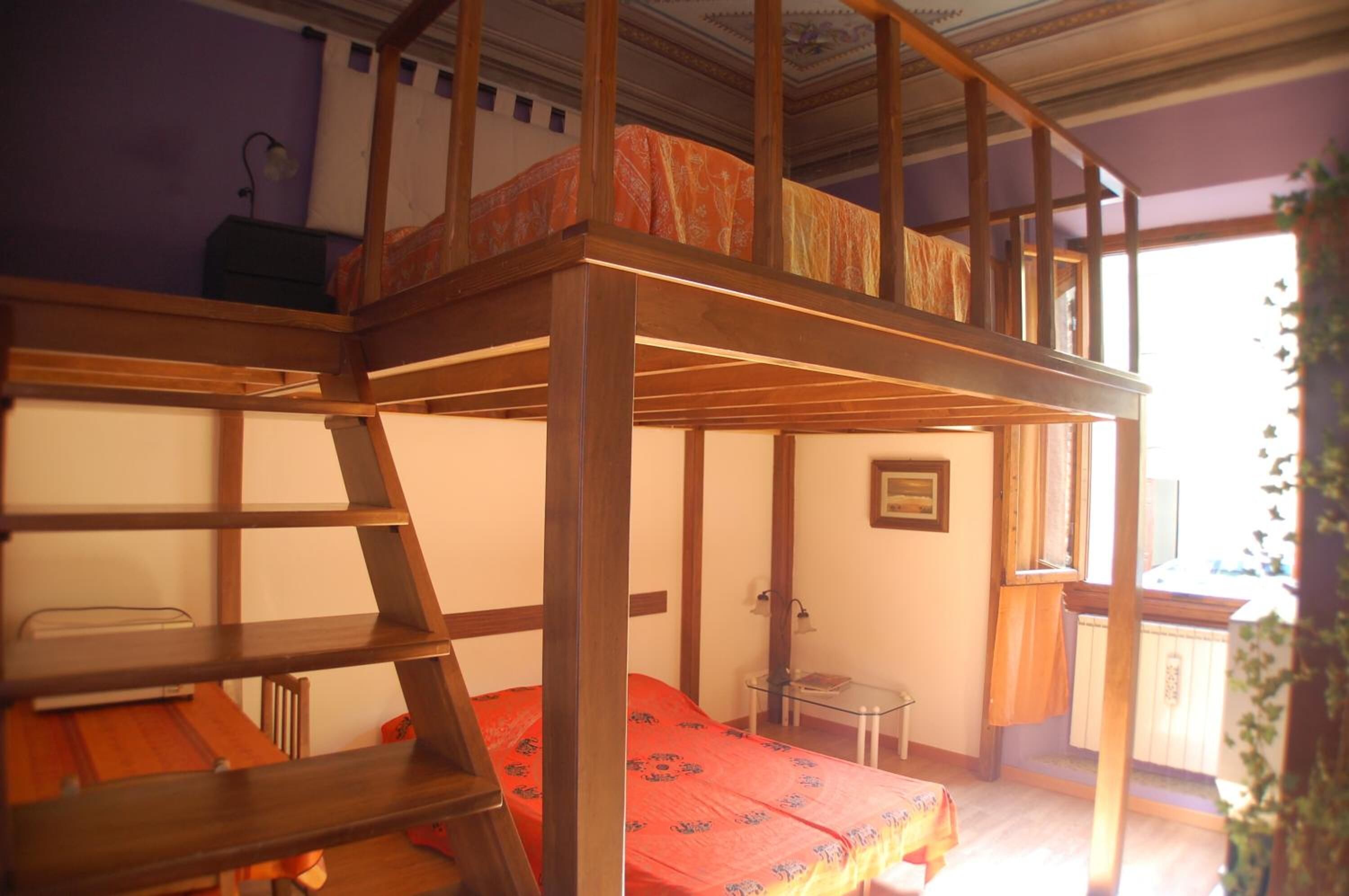 A bunk bed room with a ladder, a small table, and a window.
