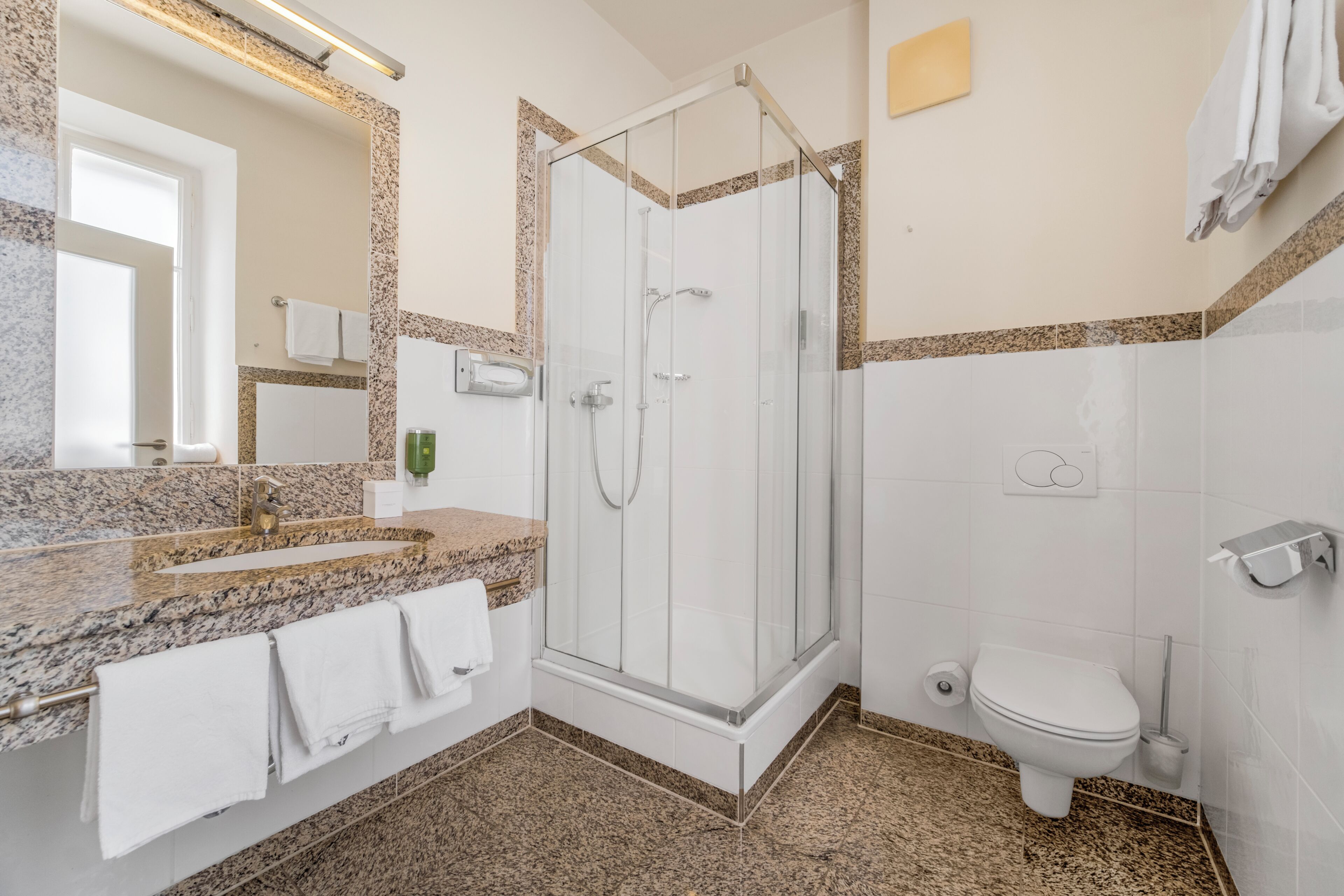 Un baño con cabina de ducha acristalada, lavabo con encimera de mármol y retrete.