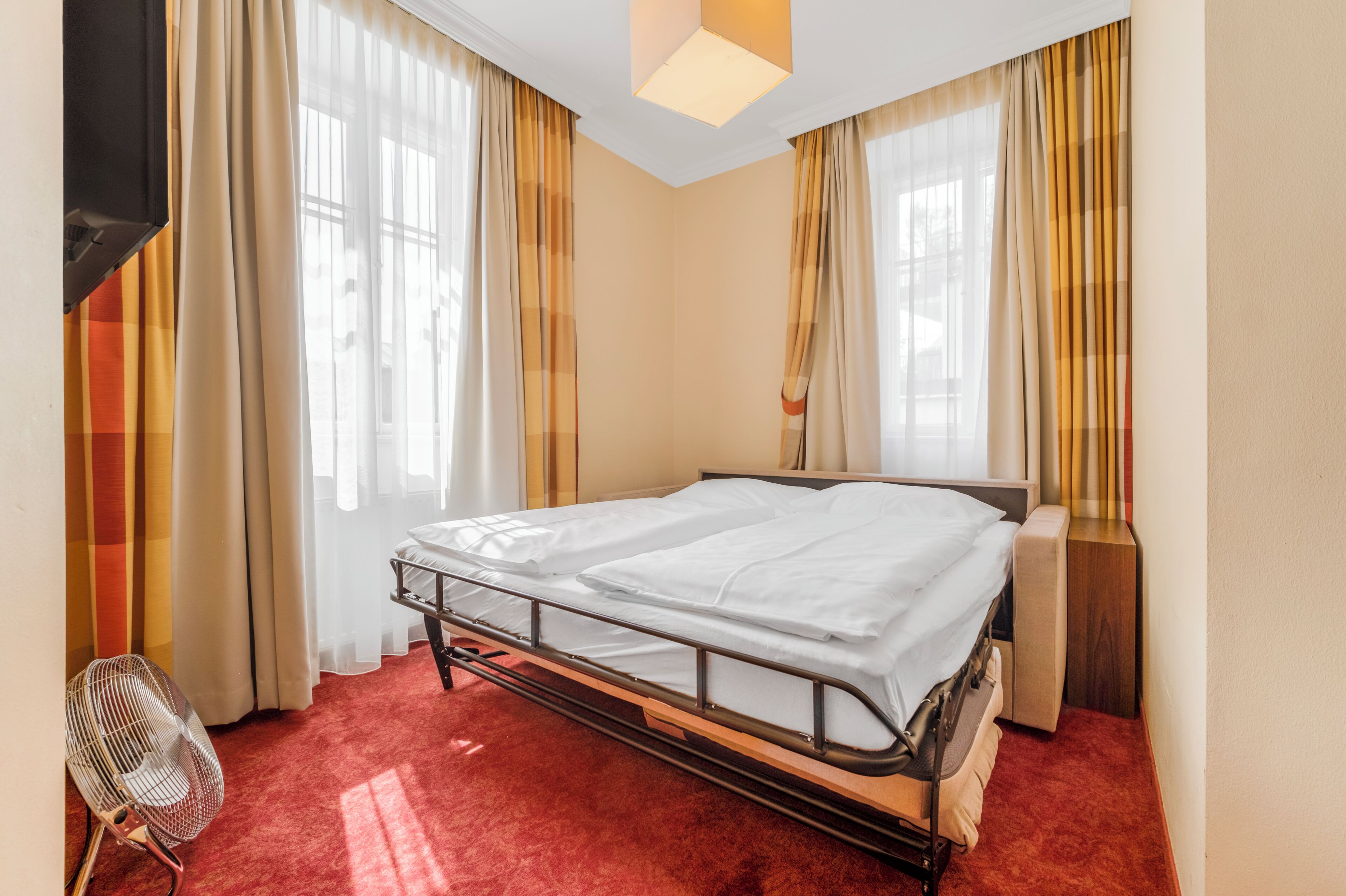 A hotel room with a bed, a chair, a bedside table, and curtains.