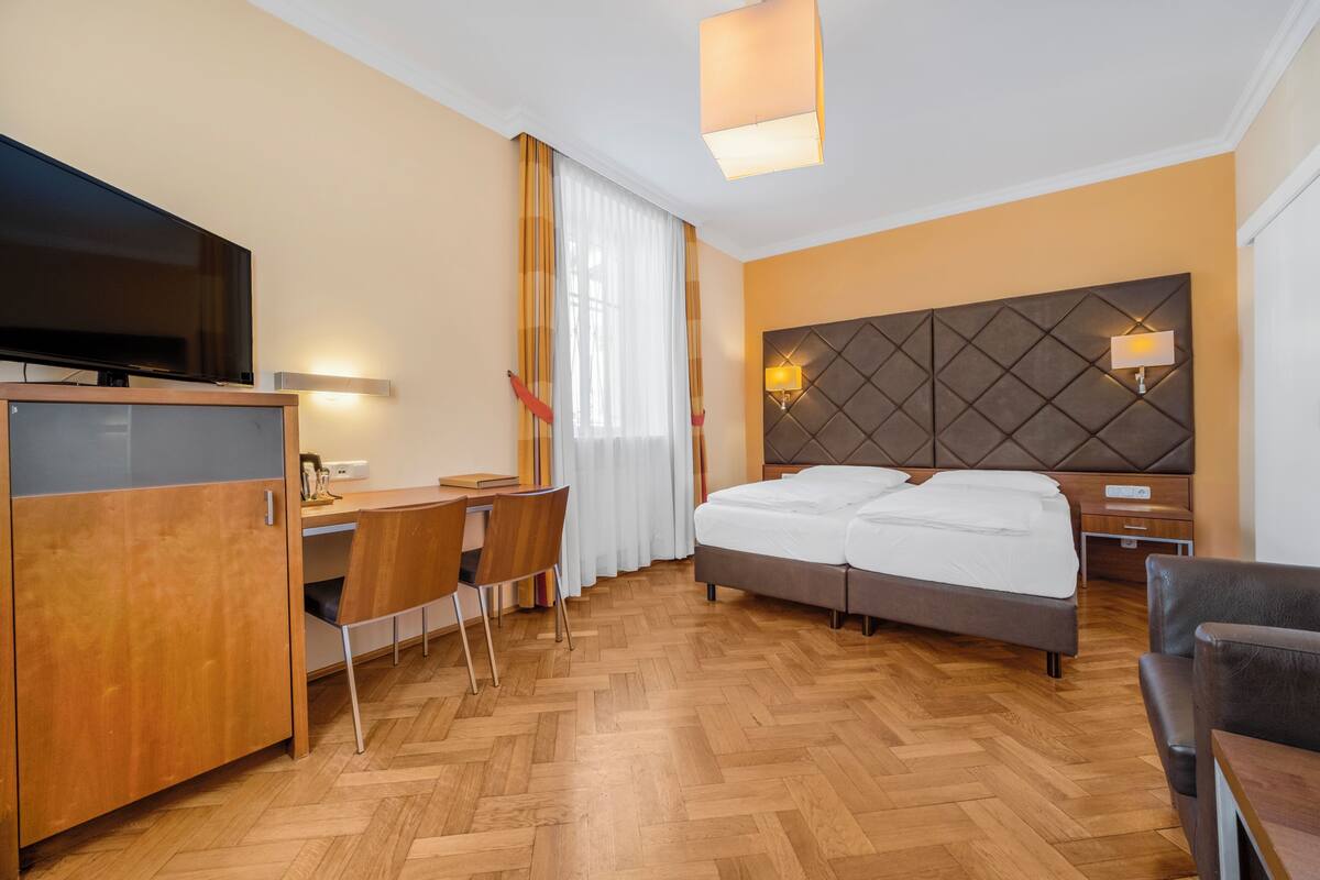 Une chambre d’hôtel équipée d’un lit, d’un bureau, d’une télévision et d’une grande tête de lit fixée au mur.