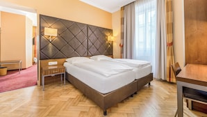 Habitación de hotel con una cama grande, una mesita de noche, una lámpara, una silla y vistas al exterior.