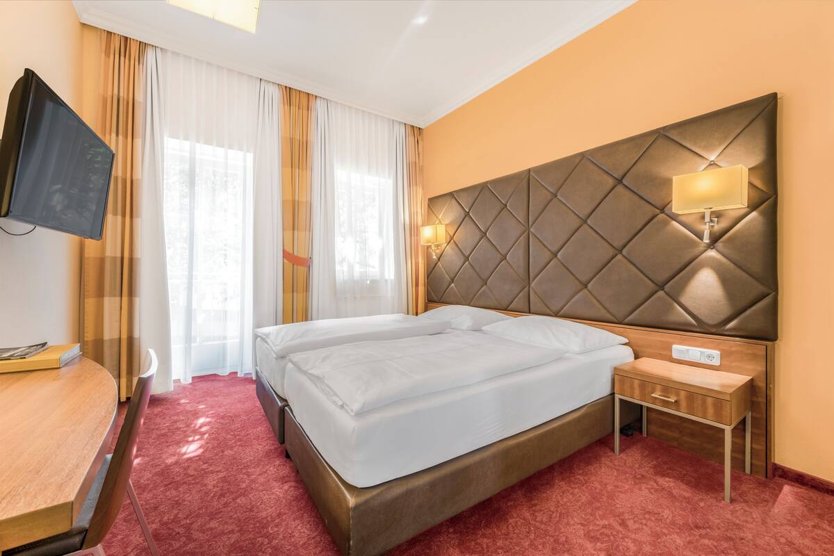 Une chambre d’hôtel avec un lit, une table de chevet, une lampe, une télévision et des rideaux.