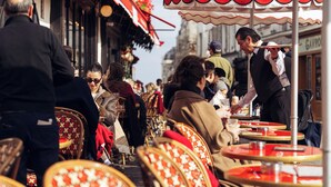 A bustling outdoor café with red and white striped umbrellas, wicker chairs, and tables. - Hotel Regyn's Montmartre (Paris)