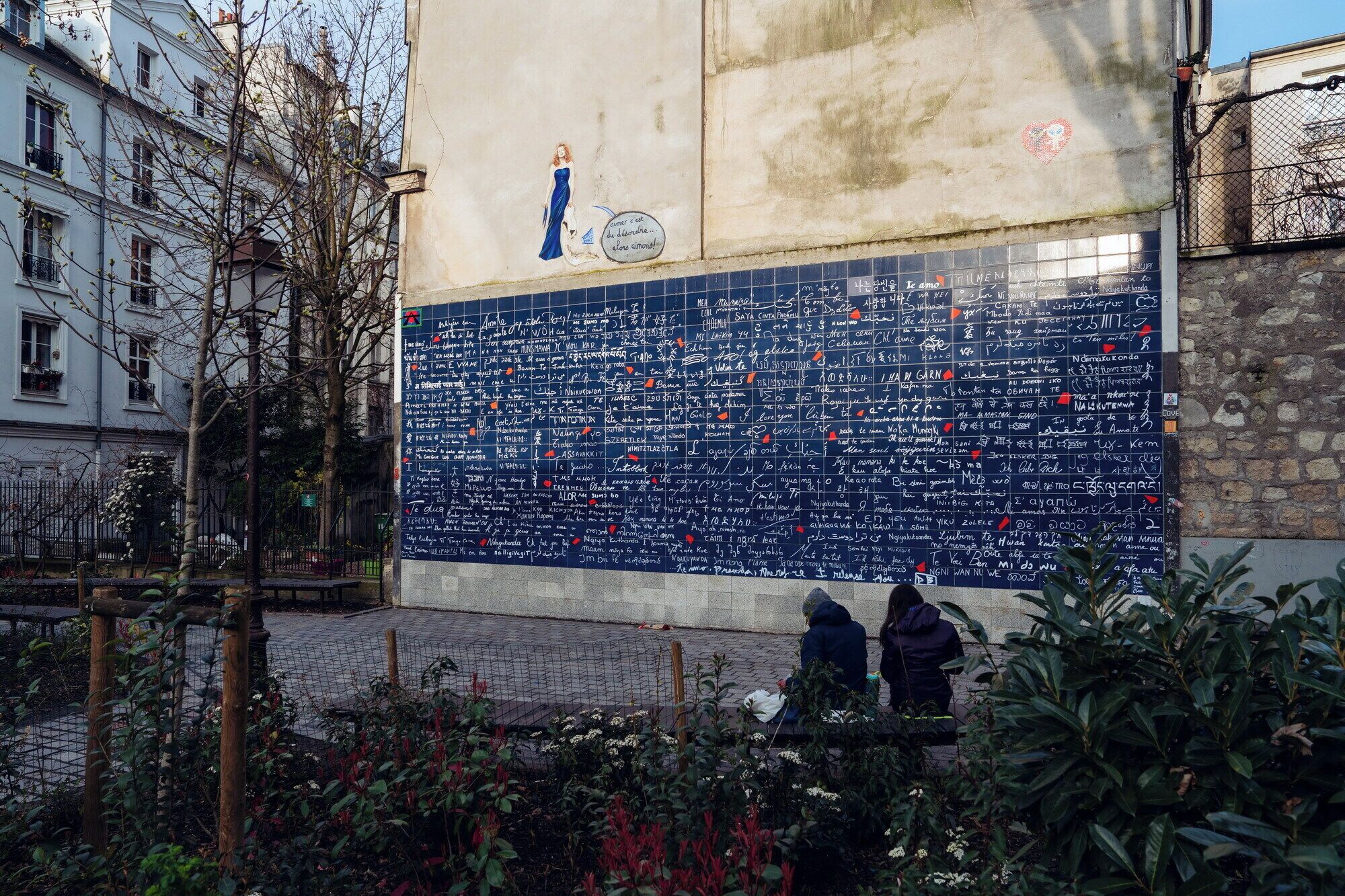 Un mur recouvert de messages écrits à la main, devant lequel sont assis deux personnes.