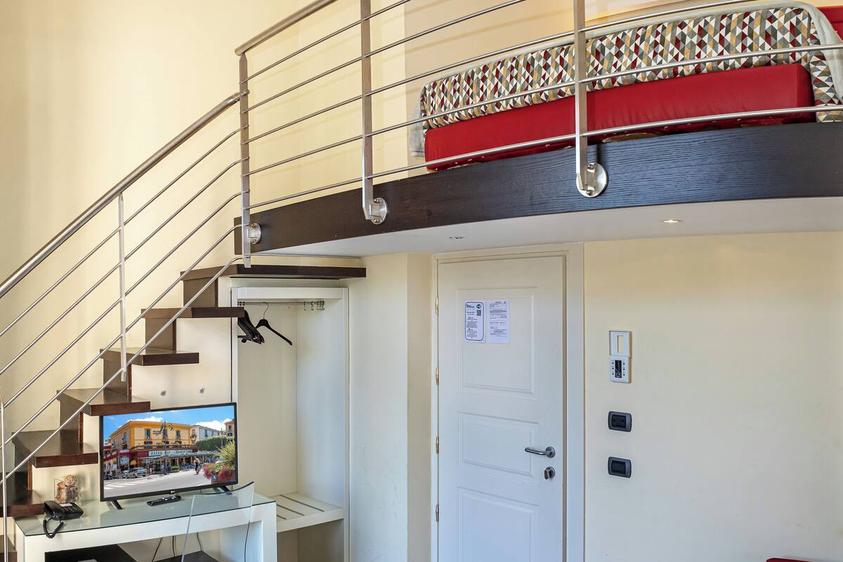 Un apartamento moderno con un escritorio de cristal, un sofá rojo, una escalera y una puerta con un aviso.