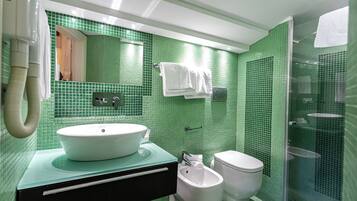 A bathroom with a green tiled wall, a white sink, a bidet, and a toilet.