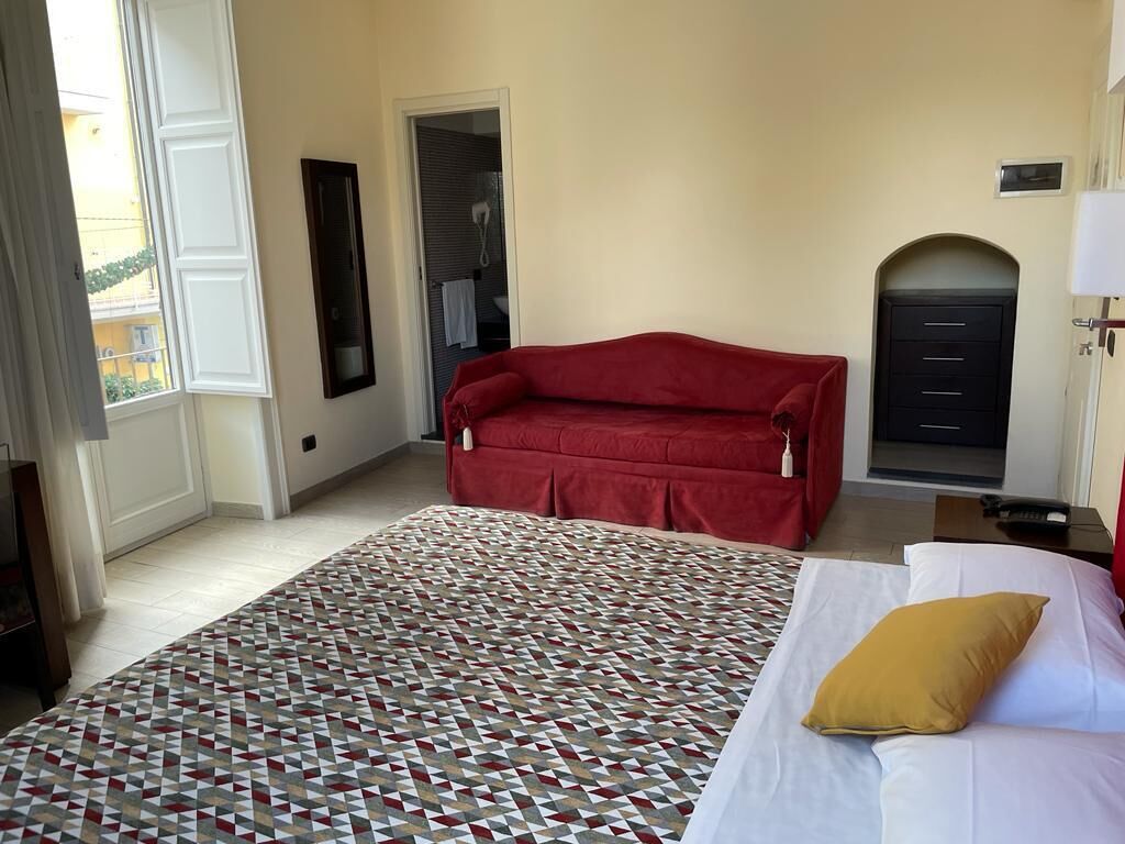 Une chambre d’hôtel avec un grand lit, un canapé rouge, un tapis à motifs et une vue sur l’extérieur.