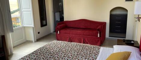 Une chambre d’hôtel avec un grand lit, un canapé rouge, un tapis à motifs et une vue sur l’extérieur.